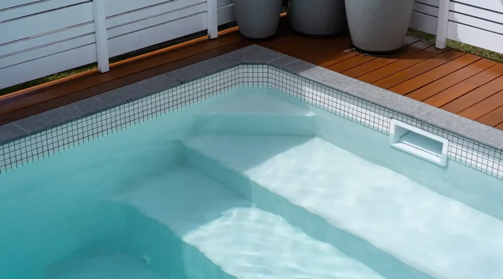 Studio pool with tile border, white privacy fence, and plants.