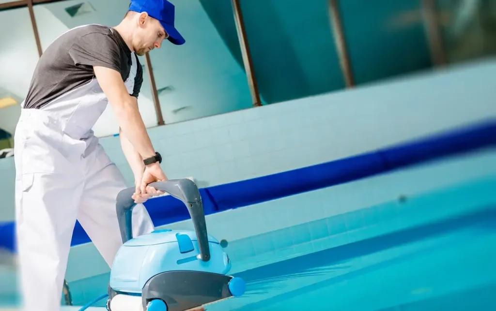 A technician handling an automated fiberglass pool vacuum cleaner by a swimming pool.