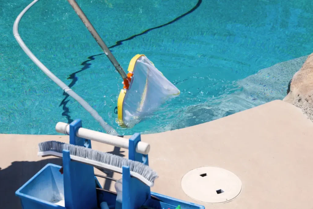 A pool maintenance net cleaning a fiberglass pool on a slope yard, with pool cleaning tools nearby.