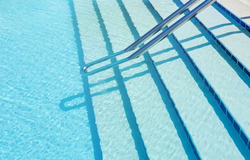 Close-up view of clear blue water in a swimming pool with ripples, highlighting concrete pool steps.