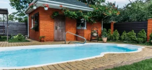 A compact fiberglass pool shell nestled in a landscaped backyard, complete with a brick pool house and vibrant greenery.