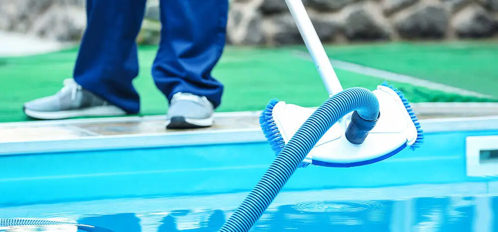 Professional pool cleaner using a vacuum hose to clean the swimming pool's floor, ensuring sparkling cleanliness.