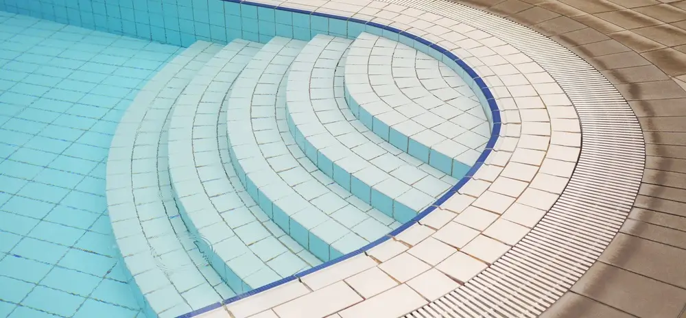 Concrete pool steps with white tiles and blue accents in a modern swimming pool, surrounded by clean poolside tiles.