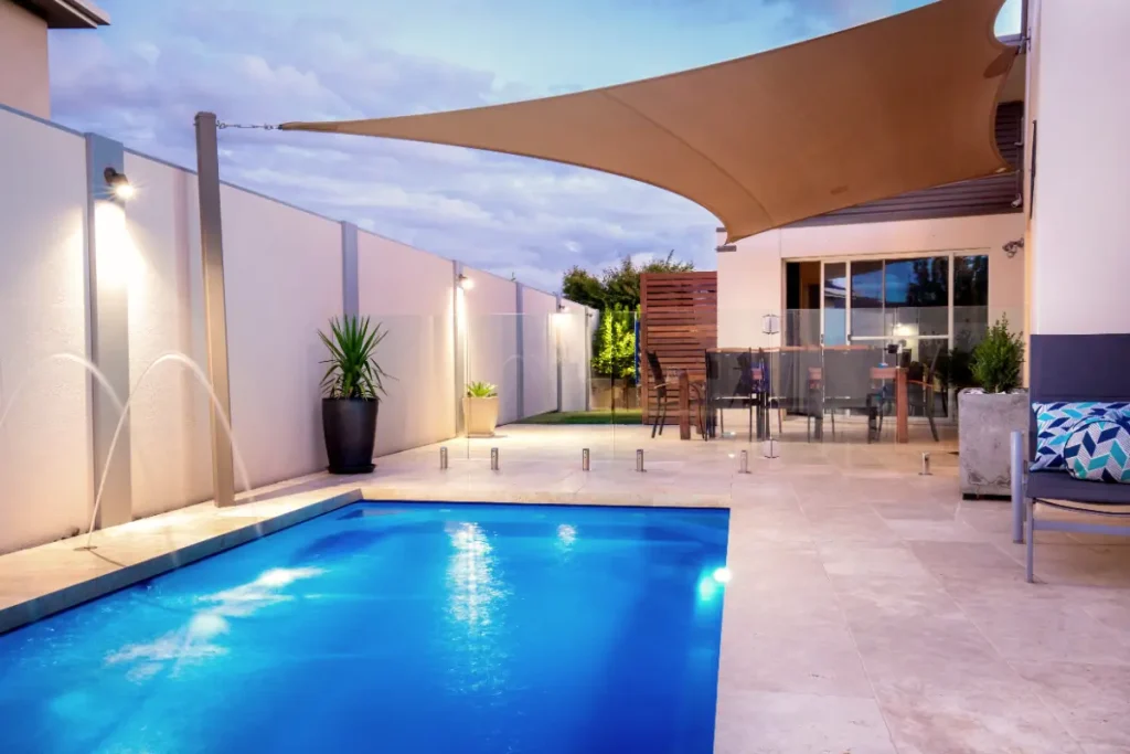 Elegant above-ground fiberglass pool with a modern patio, water features, and outdoor dining setup.