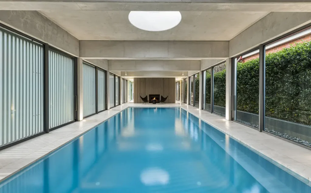 Modern indoor swimming pool surrounded by floor-to-ceiling glass windows, featuring EPS pool insulation for energy efficiency.