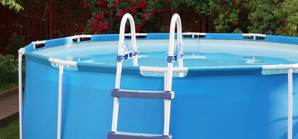 Fiberglass above-ground pool featuring an integrated hot tub and a ladder, surrounded by a garden with flowers and greenery