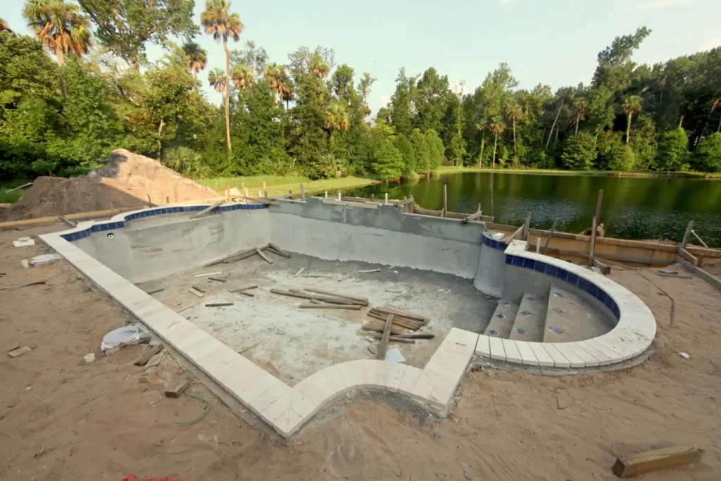 DIY fiberglass pool kit under construction near a scenic pond with tiled edges and an unfinished base.