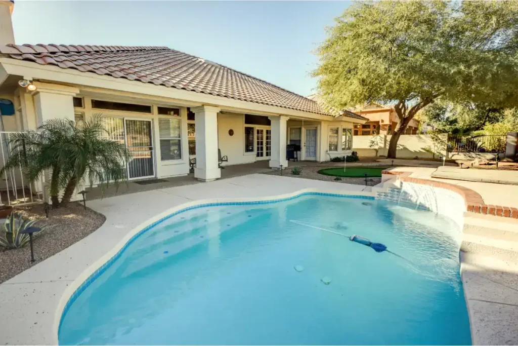 A medium fiberglass pool size surrounded by a white concrete deck, adjacent to a house with a tiled roof and outdoor seating.