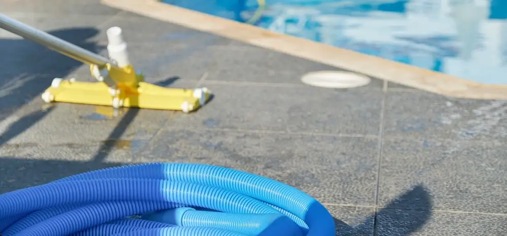 Close-up of a fiberglass pool vacuum hose and cleaning equipment beside a swimming pool.