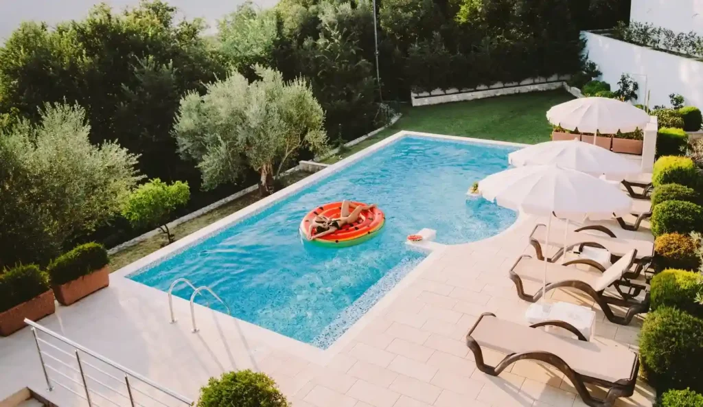 A serene fiberglass pool surrounded by lush greenery and poolside furniture, offering a perfect retreat in a sloped yard.