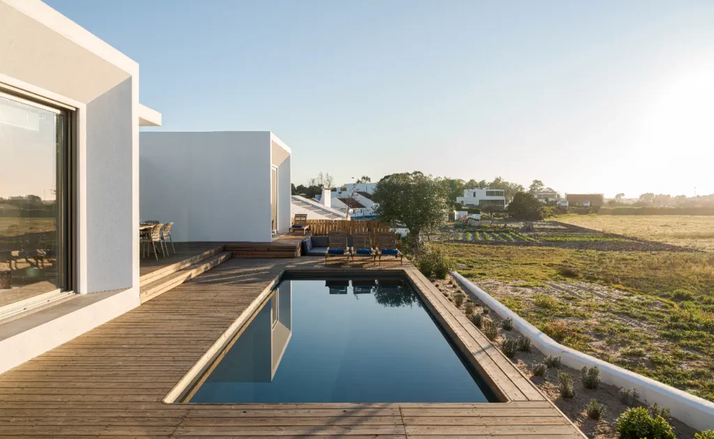 Fiberglass pool on a sloped yard surrounded by wooden decking and modern outdoor seating.