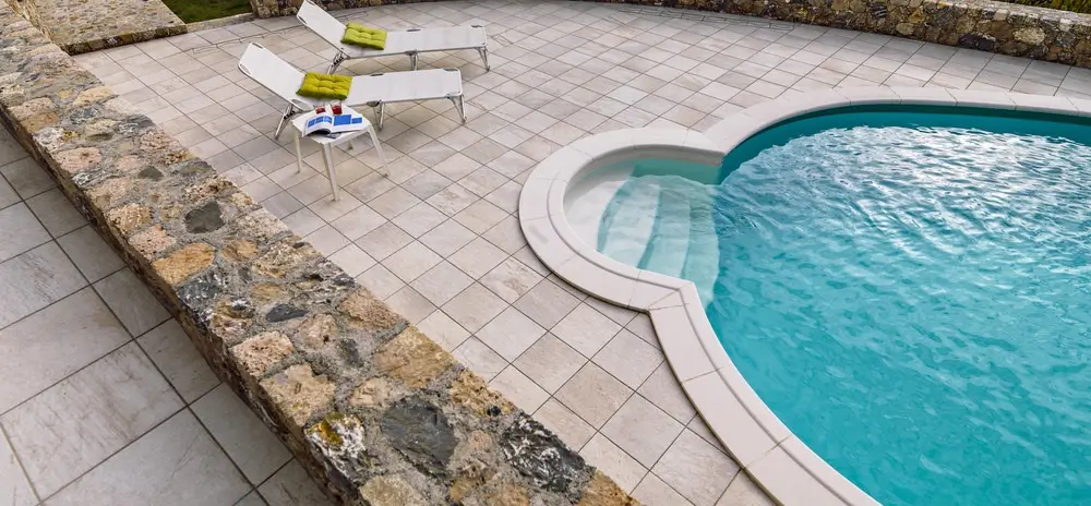 Top view of a modern fiberglass pool with surrounding tiled patio and deck chairs, highlighting durability and lifespan features.