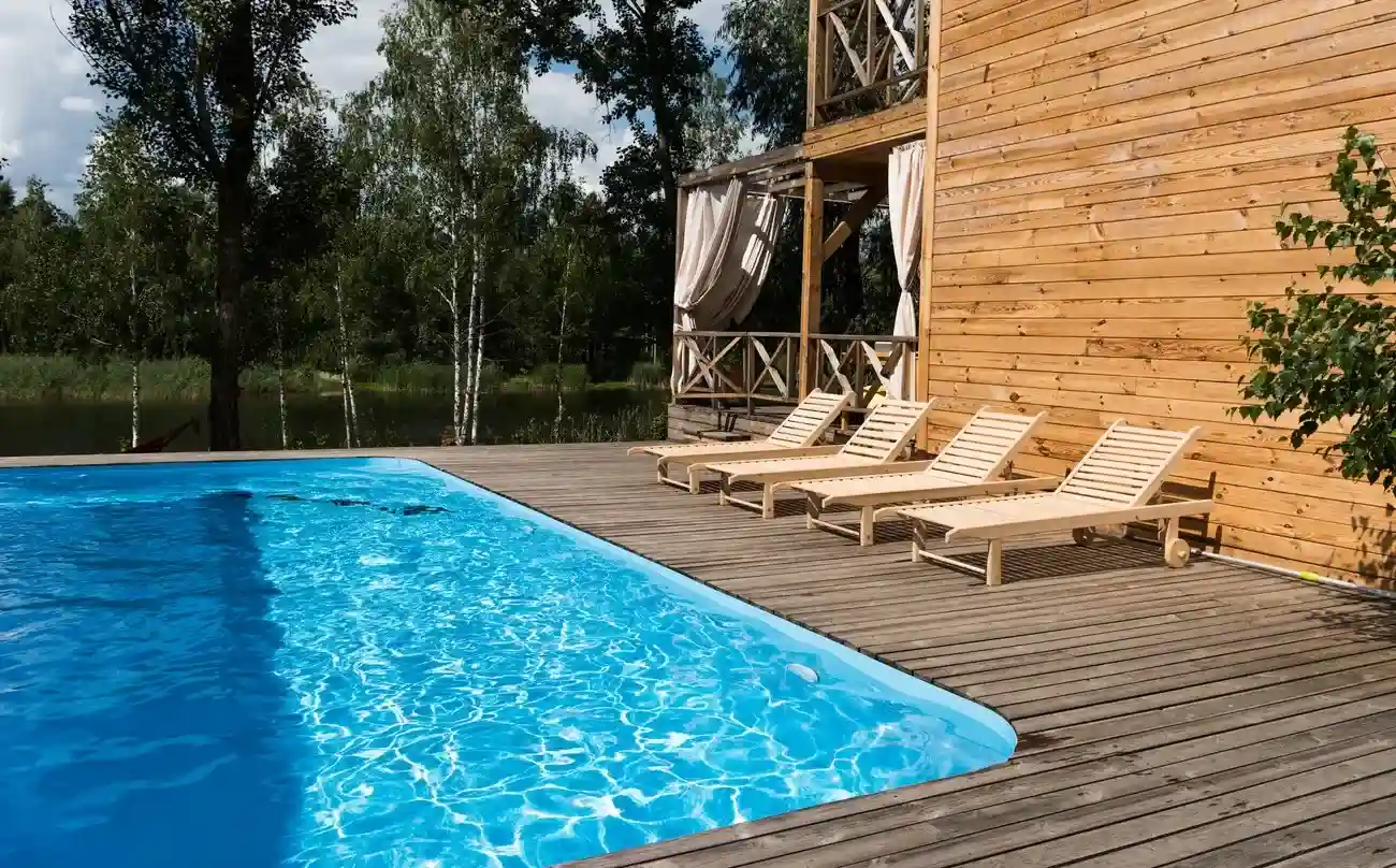 A cozy poolside view featuring a fiberglass pool shell surrounded by a wooden deck with chaise lounges under a sunny sky.