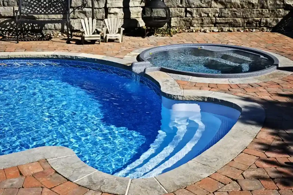 Fiberglass pool with attached hot tub and cascading water feature.