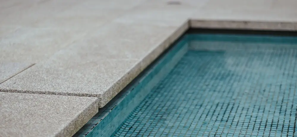 Close-up view of a concrete pool with blue mosaic tiles and stone coping, highlighting concrete pool cost considerations.