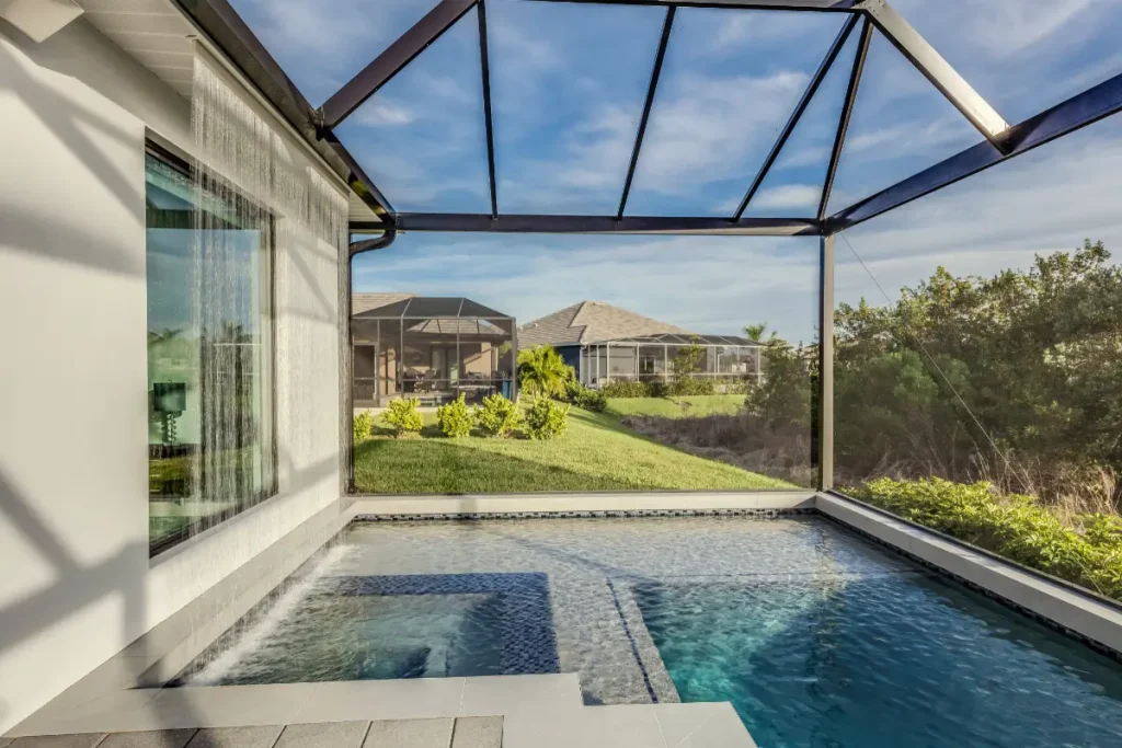 A modern fiberglass pool on a sloped yard with a screened enclosure and a cascading water feature.