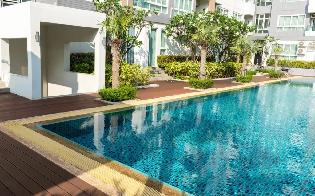 A clean outdoor fiberglass pool for sale, surrounded by lush palm trees, manicured shrubs, and a wooden deck in a modern residential setting.