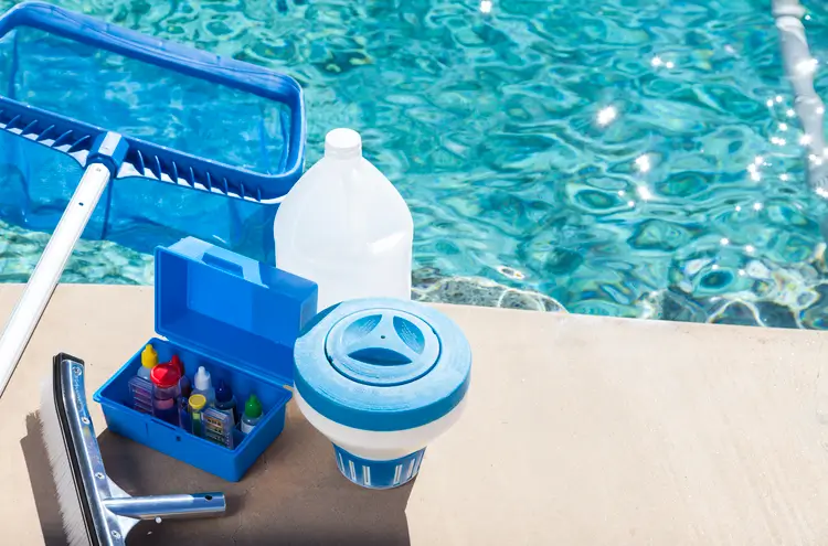 A set of pool cleaning tools and chemicals placed near a swimming pool, illustrating pool cleaning services.