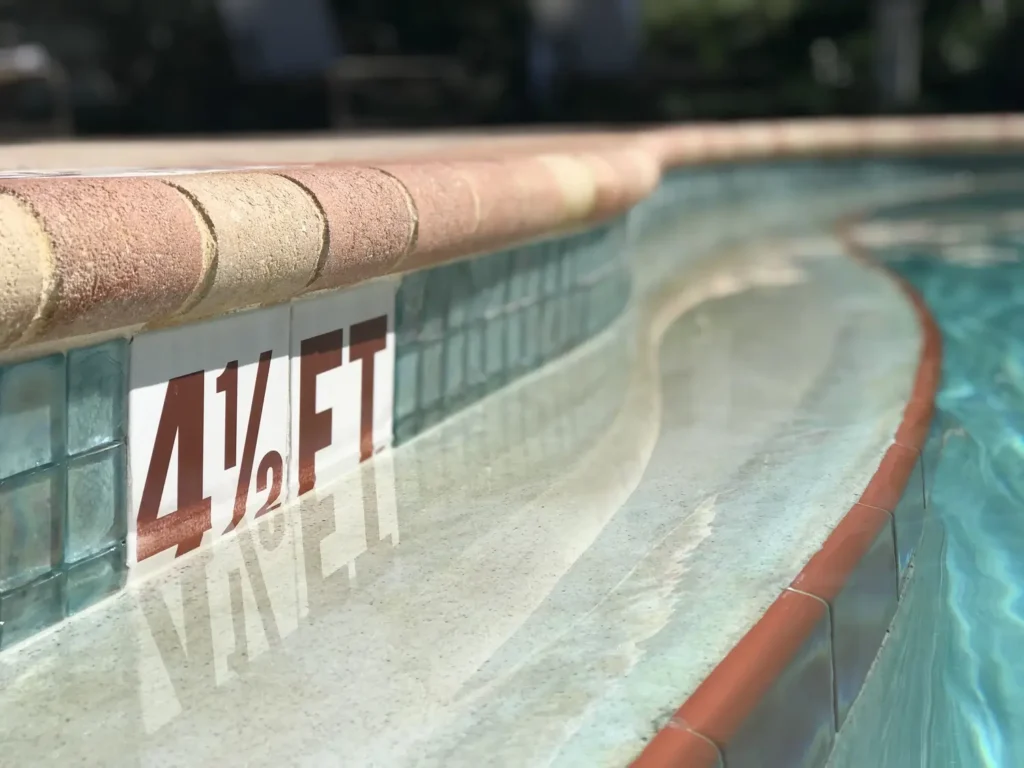 Close-up view of a swimming pool edge showing "4½ FT" depth marking with elegant tile work and clear water.