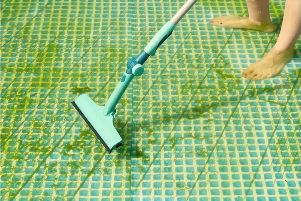 A pool cleaner using a vacuum tool to remove algae from a swimming pool floor, showcasing professional pool cleaning services.