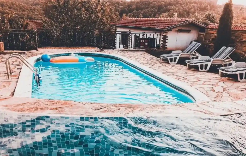 Above-ground fiberglass pool with inflatables and sun loungers in a serene outdoor setting