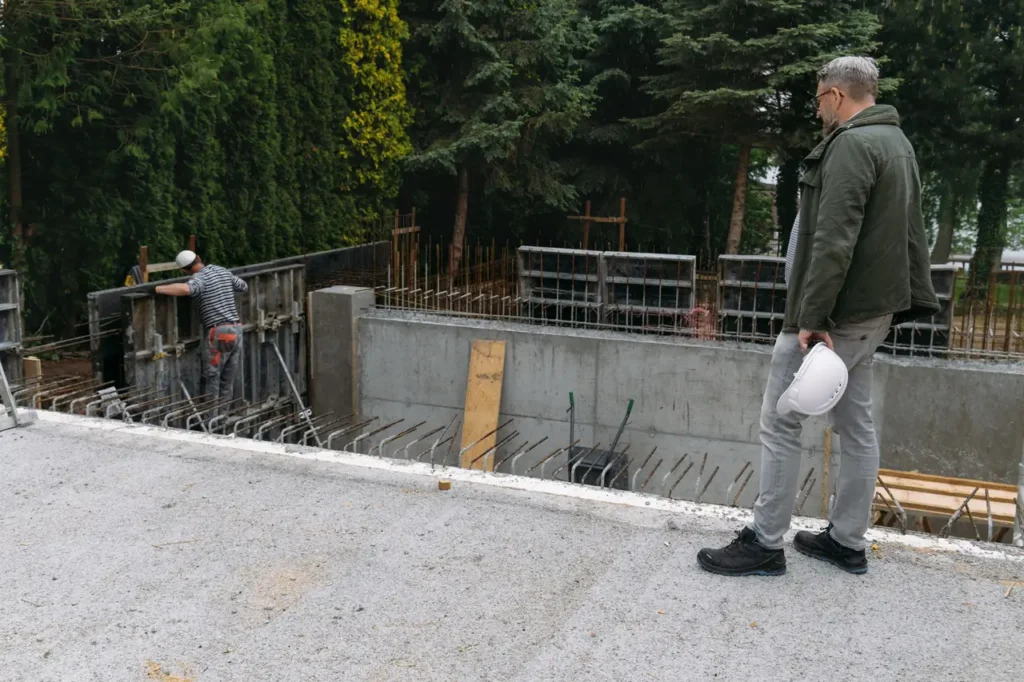 Engineer holding a helmet while observing workers building a concrete foundation for a pool, often used by fiberglass pool manufacturers