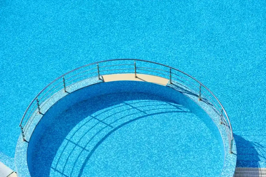 A close-up view of a circular section of an above ground pool with a metallic railing and a vibrant blue water surface.