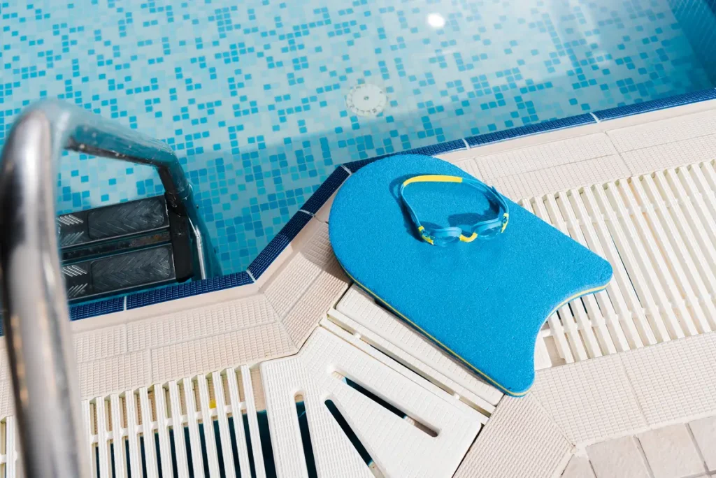 A blue kickboard with swimming goggles placed near the edge of a swimming pool, highlighting the preparation for above ground pool liner installation.