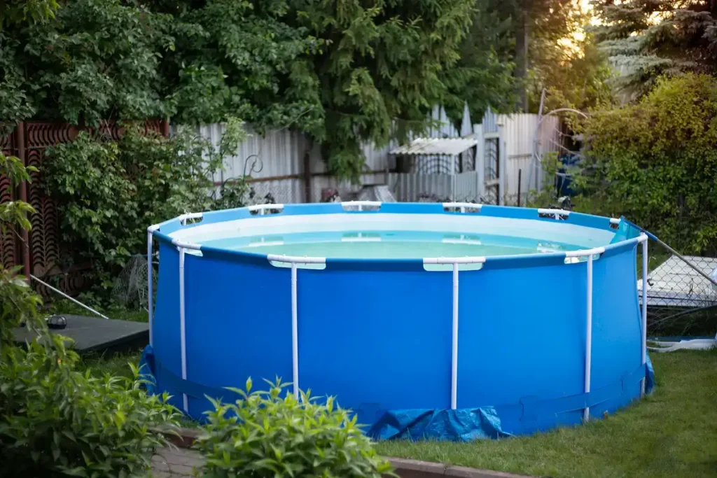 A large blue above ground pool in a backyard surrounded by greenery, illustrating above ground pool removal cost.