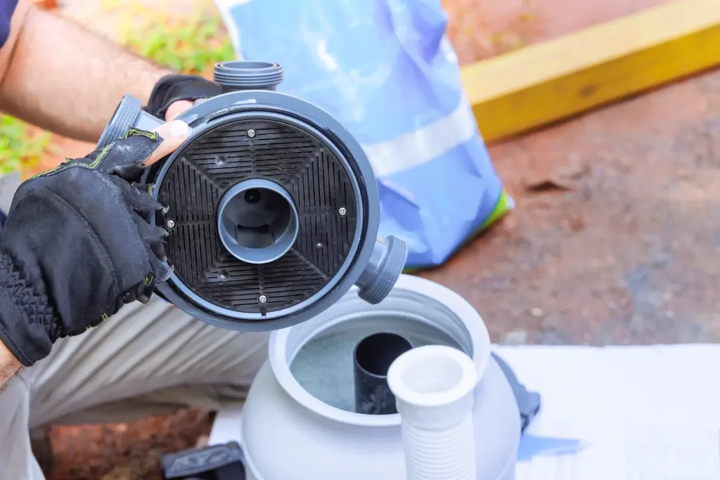 A maintenance worker assembling a sand filter tank for an above ground pool, showcasing detailed pool equipment setup.