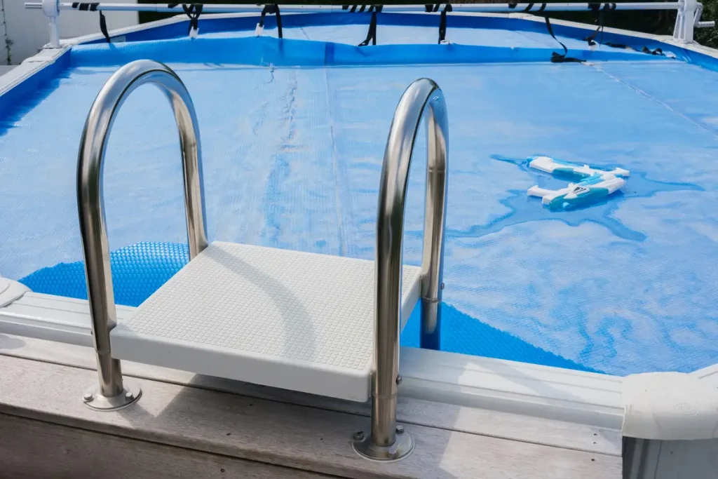 An above ground pool ladder with a white platform overlooking the pool covered in a blue liner.