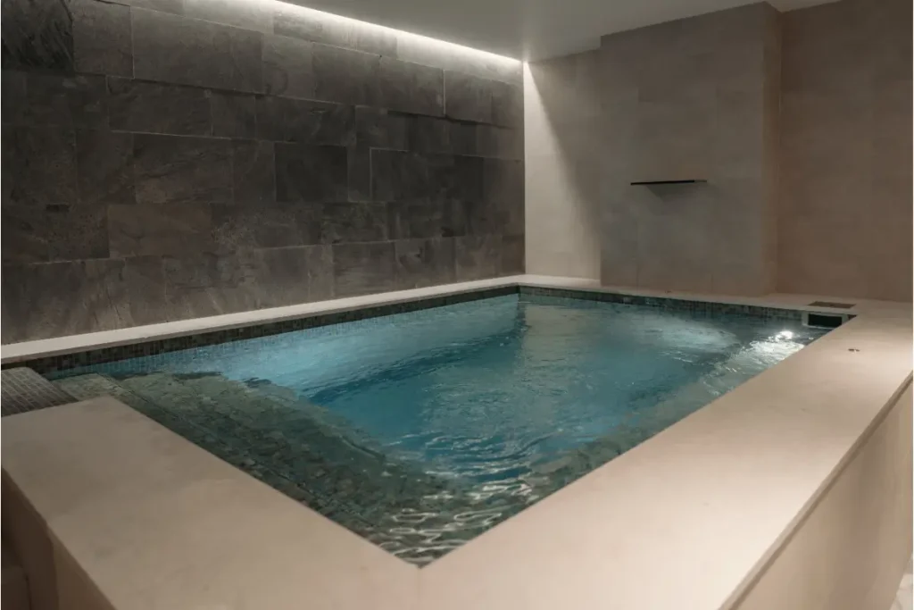 A luxurious indoor concrete pool with modern gray tile walls and water rippling, designed by an experienced concrete pool builder.