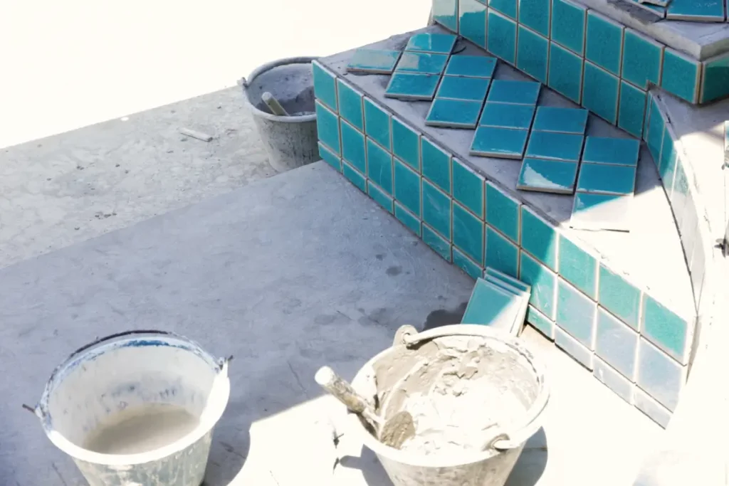 A close-up of a concrete pool under construction with blue tiles being installed, showcasing a concrete pool builder's work.