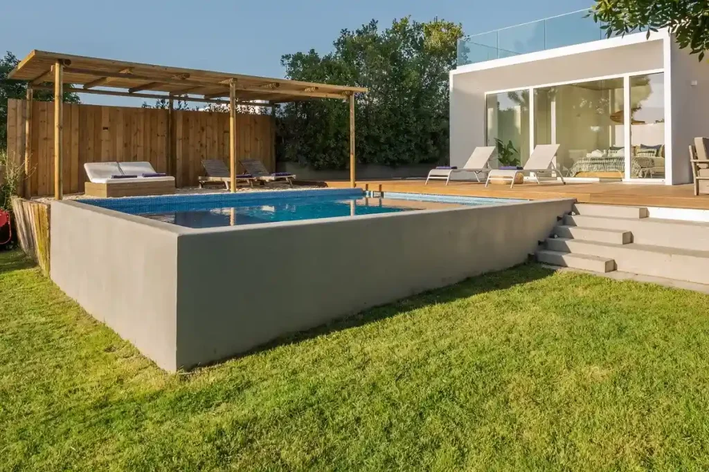 A modern villa showcasing a concrete pool above ground with a wooden deck and lounge chairs.