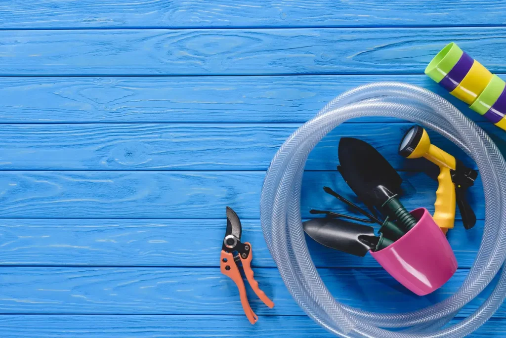 A collection of tools including a hose, pruning shears, gardening tools, and a spray nozzle, laid out on a blue wooden background, essential for above ground pool liner installation.