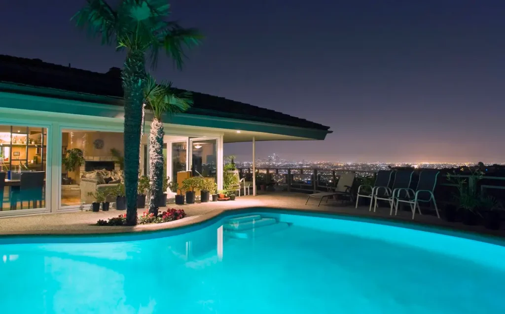 A concrete pool designed by a professional concrete pool builder, featuring a luxurious backyard and a panoramic city view at night.