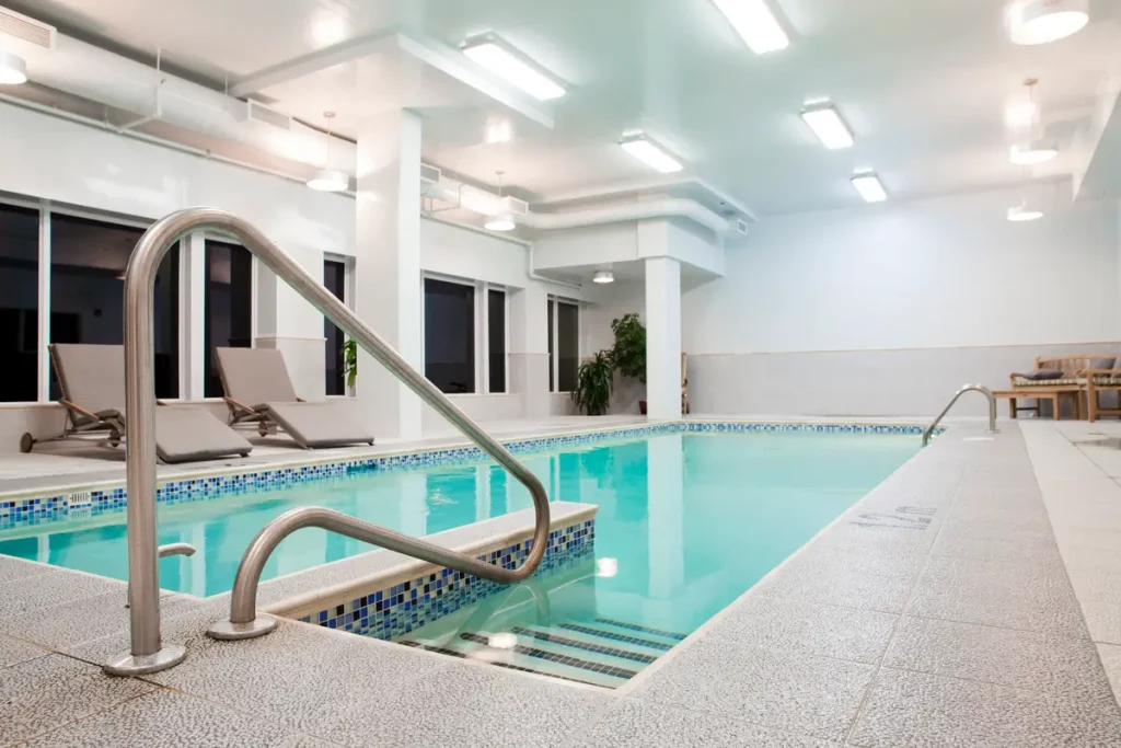 An indoor pool with a newly resurfaced concrete deck featuring smooth tiles and stainless steel handrails.