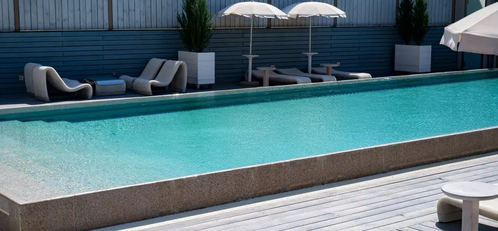 A modern concrete pool with a sleek design and surrounded by lounge chairs and umbrellas.