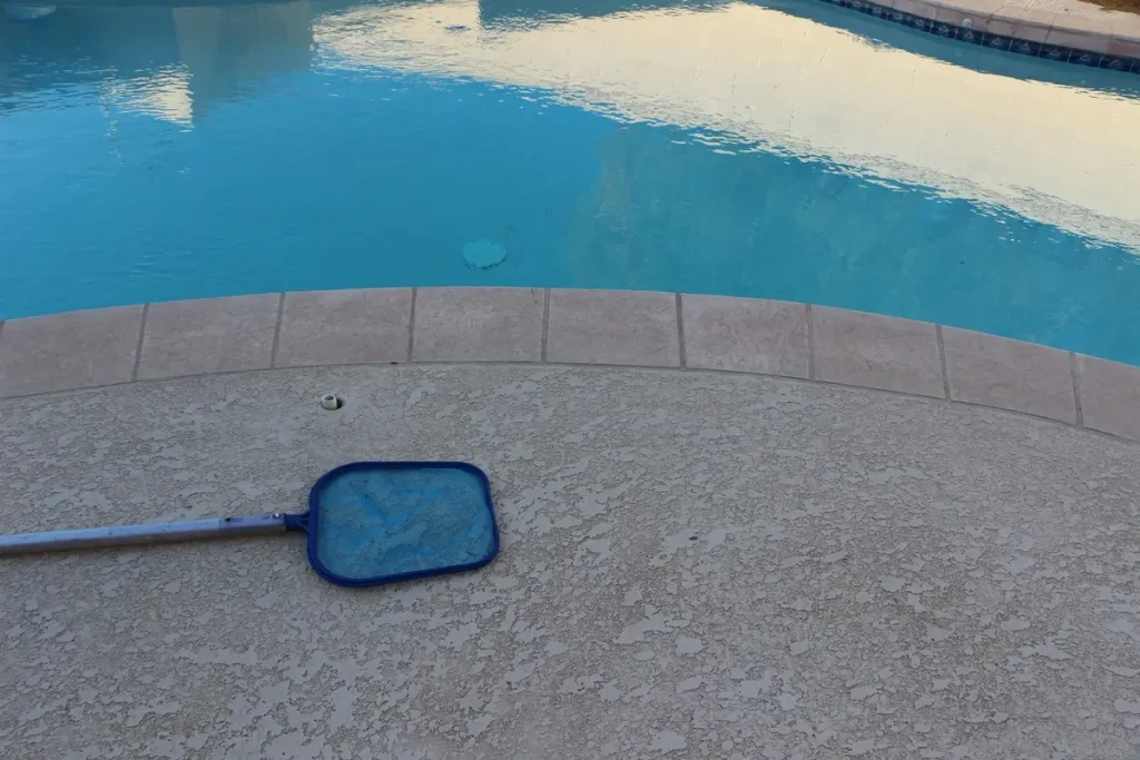 A leaf skimmer placed near the edge of a sparkling blue above-ground concrete pool.