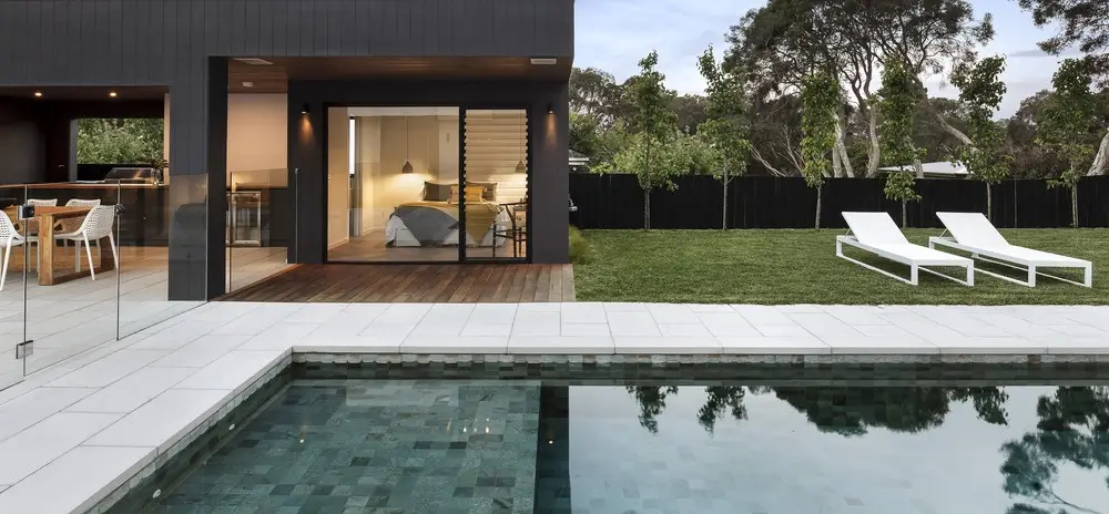 A sleek modern backyard featuring a luxurious concrete pool deck, surrounded by green lawns and contemporary outdoor furniture.