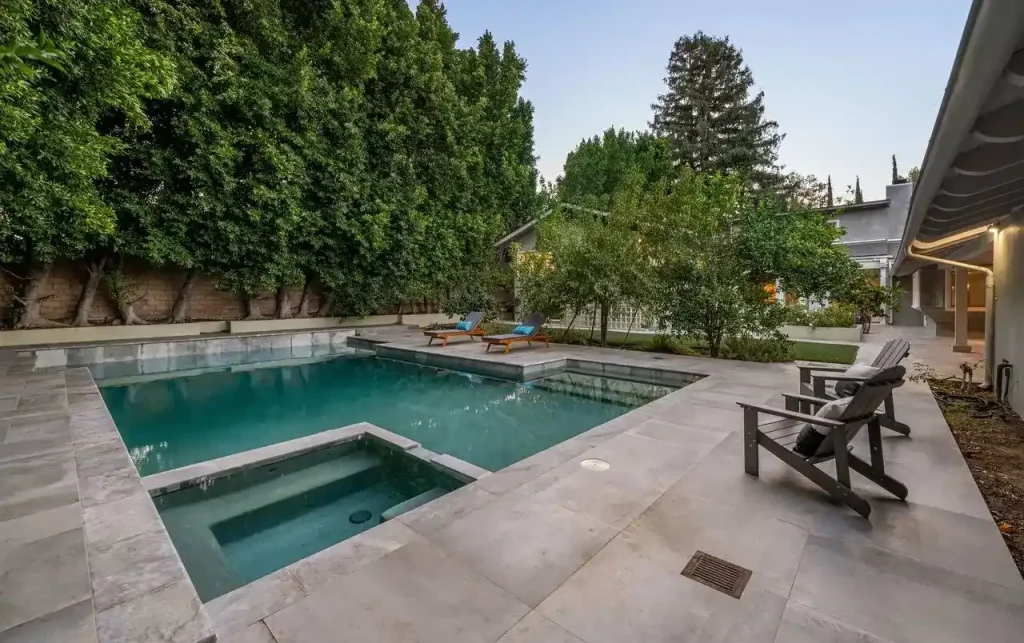 A stylish concrete pool with a built-in hot tub, surrounded by greenery and modern outdoor furniture, offering a glimpse into the value of concrete pool cost.