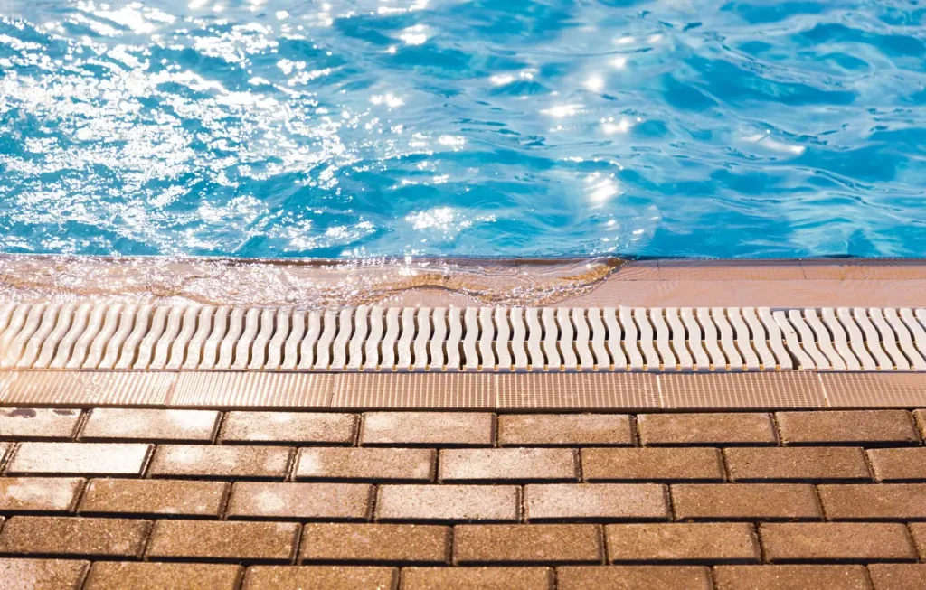 Close-up of an above ground pool deck edge with drainage grates and clean blue water.