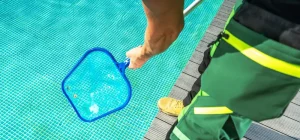 A person using a manual skimmer to clean debris from an above-ground swimming pool.