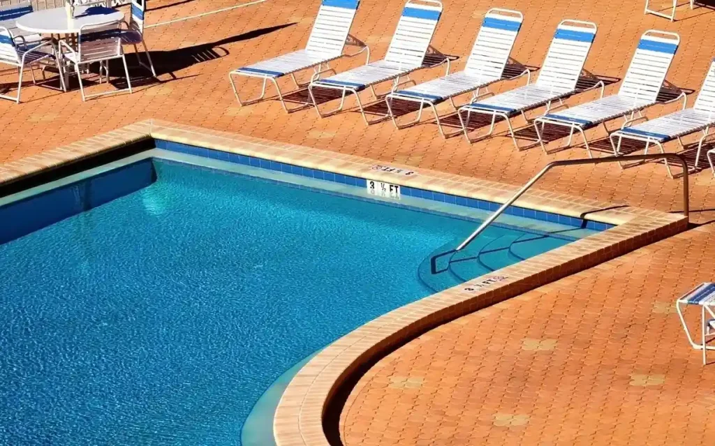 A bright poolside area featuring lounge chairs on a concrete pool deck, perfect for a sunny day outdoors.