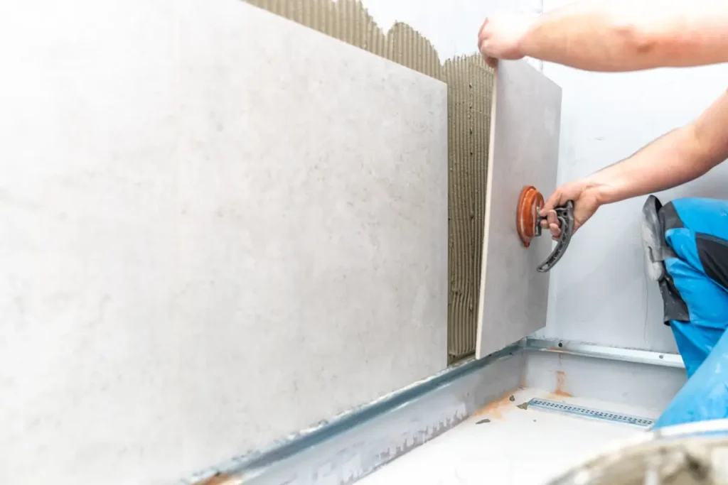 Worker installing large-format tiles on the pool wall as part of an above ground pool setup.