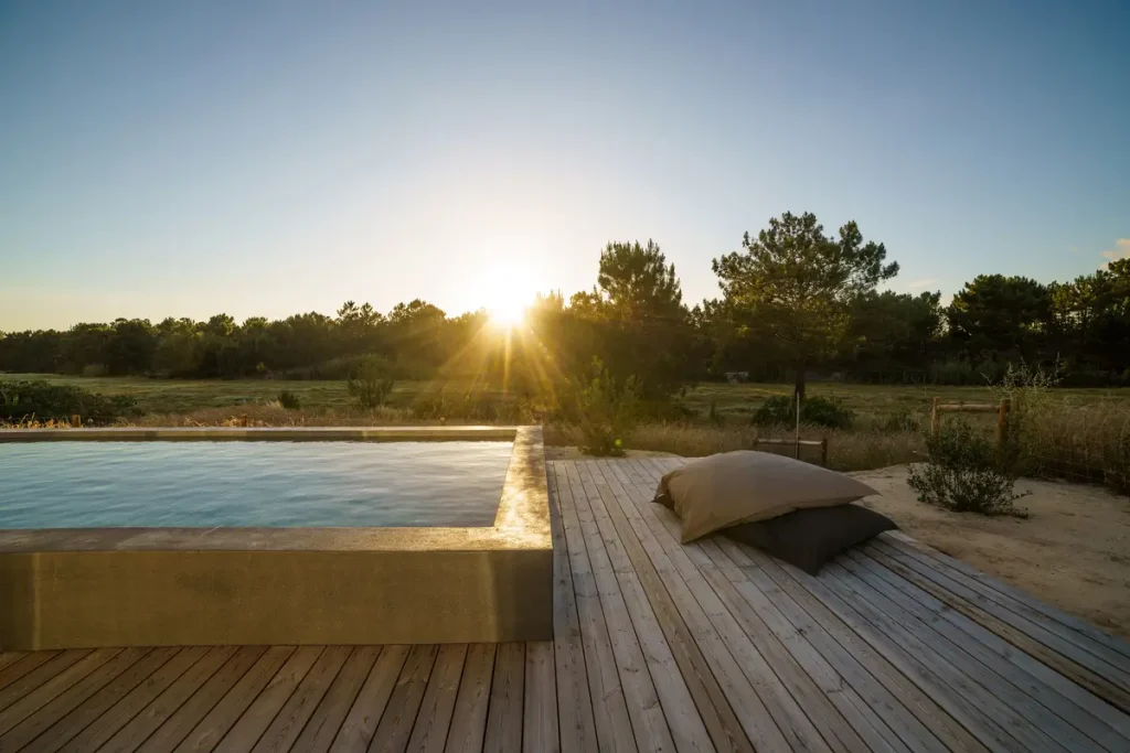 Above ground pool deck ideas with wooden flooring, large cushions, and a scenic sunset landscape.