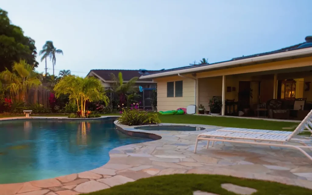 A peaceful backyard with a freeform swimming pool surrounded by a natural stone-inspired concrete pool deck and lush greenery, perfect for relaxation.