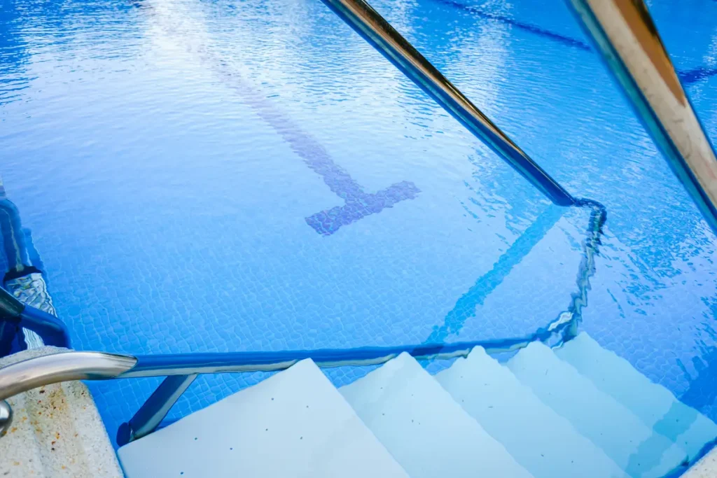 Steps leading into a crystal-clear swimming pool with handrails for added safety.