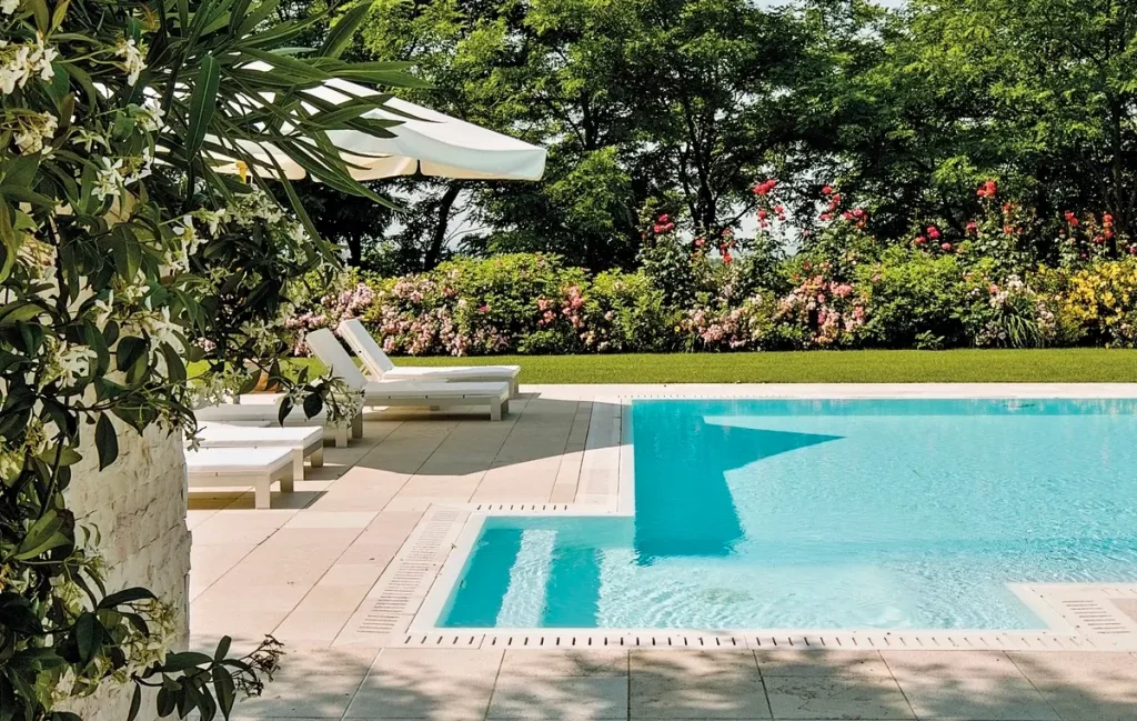 Lush garden surrounding a fiberglass pool with lounge chairs and umbrellas.