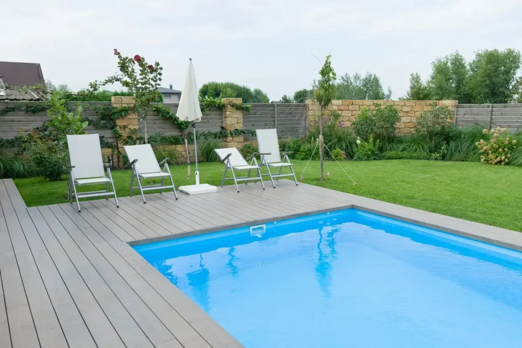 Above ground pool deck surrounded by a green lawn with lounge chairs and an umbrella.